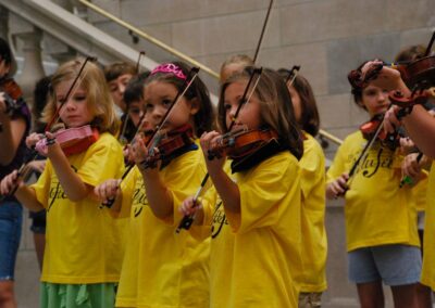 Young performers in yellow shirts play their violins while standing