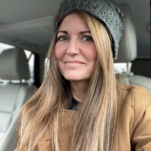 Karen Freidt in a gray hat and tan coat sits in her car